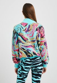 Farverig, blød sweater med flerfarvet dyreprintdesign i nuancer af blå, pink, lilla og guld, kombineret med stribede leggings.