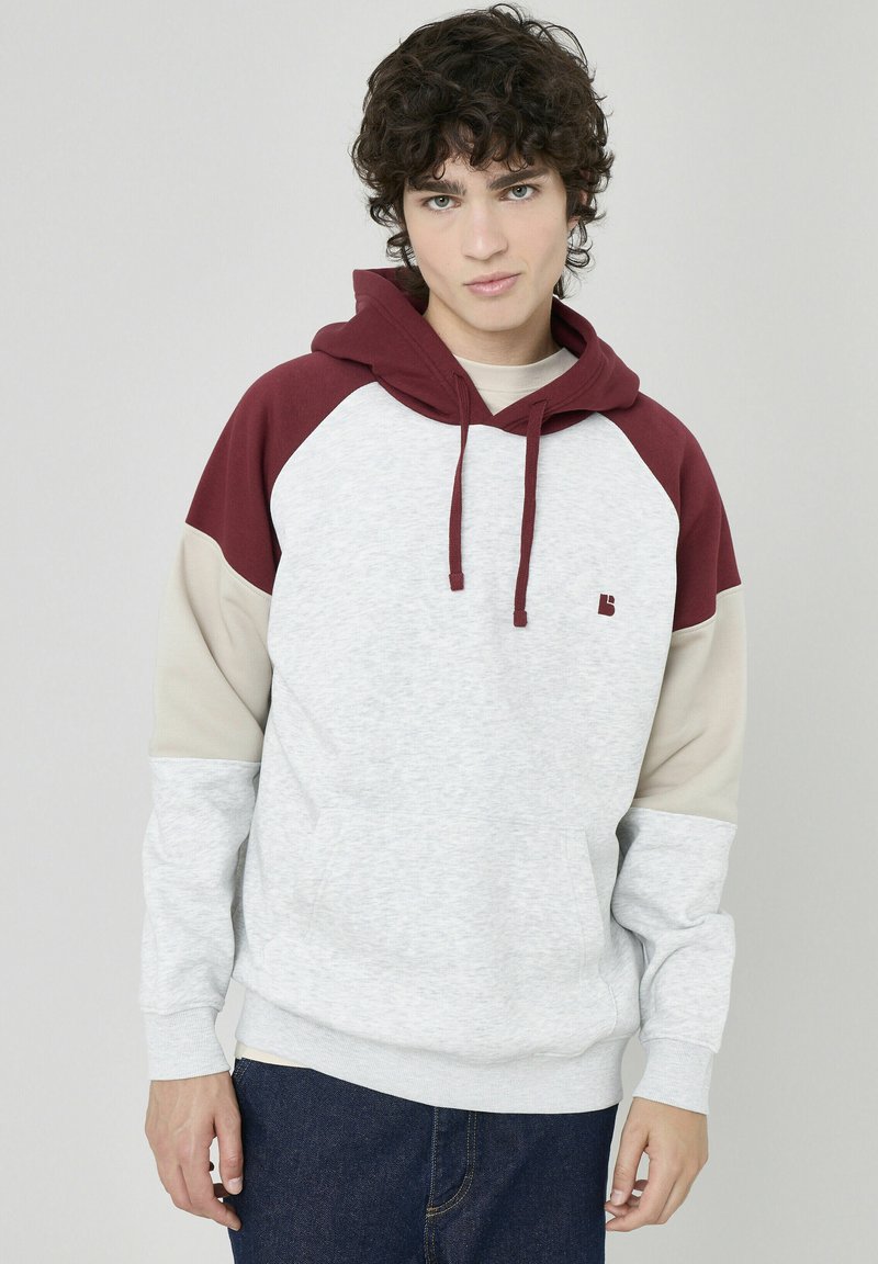 Sweat à capuche avec un corps gris, des manches bordeaux et beige. Comprend une poche kangourou à l'avant et des cordons de serrage. Tissu en mélange de coton doux.