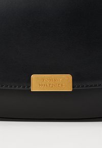 Borsa a tracolla in pelle nera con una placca in tonalità oro e logo in rilievo. Texture liscia con cuciture minime e un design elegante.