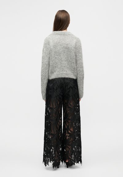 Γκρι χνουδωτό πουλόβερ σε συνδυασμό με μαύρο παντελόνι φαρδιάς μπατζάκι από δαντέλα με μοτίβο φύλλου, που αναδεικνύει τη διαφάνεια και τις περίπλοκες λεπτομέρειες.