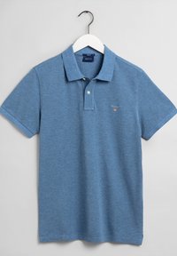 Ljusblå pikétröja i texturerad bomull, med klassisk krage, treknappsgärde och liten broderad logotyp på bröstet.