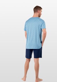 Camicetta azzurra a maniche corte con un motivo a rombi, abbinata a pantaloni corti navy. Materiale in misto cotone, vestibilità ampia e leggera texture.
