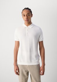 Witte geribbelde gebreide polo met een kraag en drie knopen, met korte mouwen en een effen gebreid lichaam, gedragen met beige broek.