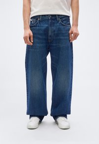 Φαρδιά μπλε τζιν από denim, με ίσια γραμμή παντελονιού, διακριτική ξεθώριαση, εμπρόσθιες τσέπες και φερμουάρ με κουμπί κλεισίματος.