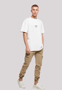 White short-sleeve T-shirt with black print, paired with beige cargo pants featuring pockets and elastic cuffs. Worn with white sneakers.