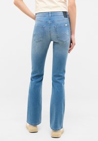 Jeans acampanados de color azul claro con cintura alta, que cuentan con dos bolsillos traseros con un sutil diseño de ola y una etiqueta de cuero en la cintura.
