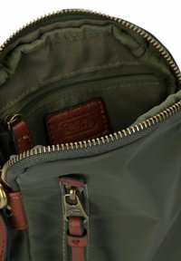 Dunkelgrünes Stoffbeutel mit einem hellbraunen Lederetikett, Reißverschluss in Goldoptik und mehreren Taschen. Glatte Textur mit verstärkten Nähten.