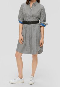 Robe chemise à rayures noires et blanches avec une taille ceinturée, des manches courtes et des accents bleus sur les poignets. Associée à des baskets blanches.