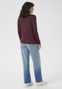 Lange ermer burgunder topp, tettsittende ved skuldrene, kombinert med lys blå vide jeans. Mykt stoff med jevn tekstur og minimalistisk design.