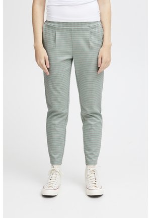 Grüne karierte Hose mit lockerem Schnitt, ausgestattet mit vorderen Falten und Seitentaschen. Kombiniert mit weißen Sneakern für einen lässigen Look.