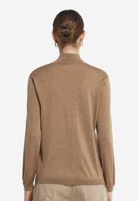 Brun långärmad stickad tröja med hög krage och ribbade muddar. Tyget verkar mjukt och har en jämn struktur.