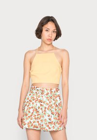 Top amarelo cropped com design de alças, combinado com calções brancos com um padrão de frutas laranja e verde. Tecido suave, ajuste descontraído.