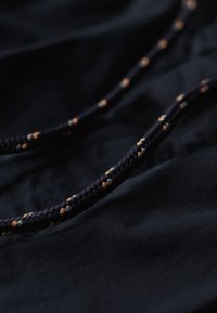 Tela negra con detalles de cuerda trenzada que presenta acentos en naranja, gris y blanco, creando una apariencia texturizada y con capas.
