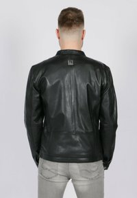 Chaqueta de cuero negra con una textura suave, diseño ajustado y una pequeña etiqueta con el logo en la parte trasera, mostrada desde atrás.