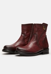 Bottes en cuir bordeaux jusqu'à la cheville, avec une fermeture éclair latérale, un bout rond, une finition texturée, et un bouton décoratif en métal sur le côté extérieur.