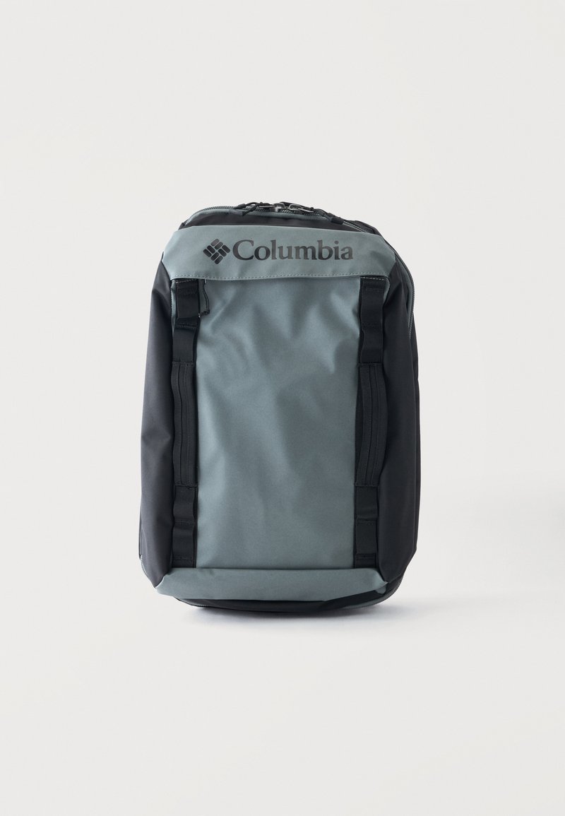 Γκρι και μαύρο σακίδιο Columbia με επάνω φερμουάρ και μπροστινούς ιμάντες, όρθιο σε λευκό φόντο.