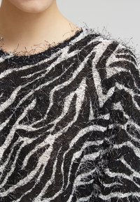Svetr s černobílými pruhy s chlupatou texturou, který má vzor zebra a volný, oversized střih. Jsou viditelné upravené okraje.