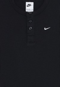 Črna majica iz waffle tkanine Nike z enim črnimi gumbi in belim vezenim logotipom Nike na prsih.