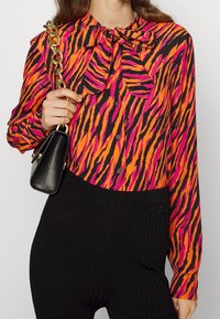 Felle oranje en roze zebra-gestreepte blouse met een strikzoomkraag, knoopsluiting en lange mouwen; gecombineerd met zwarte geribbelde onderkleding.
