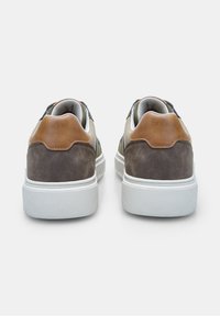 Tenisi cu un corp din suede gri, accente din piele maro și tălpi din cauciuc alb. Prezintă un design low-top și vârf rotund.