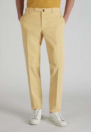 Pantalons jaune clair en coton avec une coupe droite, dotés de poches latérales et d'une texture lisse, assortis à des baskets blanches.