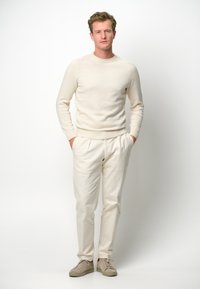 Helle cremefarbene Strickjacke mit gerippten Bündchen, kombiniert mit hellbeigen Faltenhosen und beigen Sneakern. Einfaches und sauberes Design.