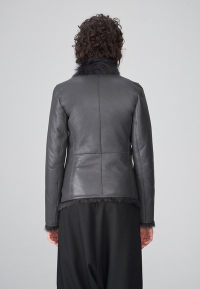 Chaqueta de cuero negra con un cuello y puños de pelaje texturizado. Diseño ajustado, costuras rectas y una cintura ligeramente ceñida, se muestra vista trasera.