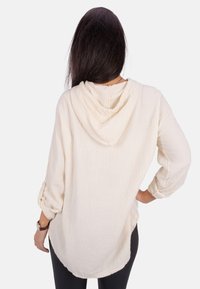 Helle beige Kapuzenbluse aus strukturiertem, zerknittertem Stoff. Mit hochgerollten Ärmeln und abgerundetem Saum. Weiches, lässiges Design.