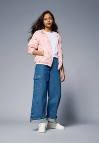 Light pink zip-up jacket with polka dots, white t-shirt, wide blue denim cargo pants, and white sneakers. Smooth fabric, casual fit.