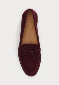 Burgundy suede moccasin shoe with a rounded toe, decorative stitching, and a flat rubber sole. Features a cushioned insole for comfort.