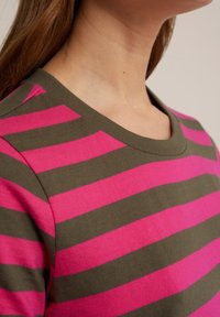 Bomullsskjorta har horisontella ränder i fuchsia och olivgrön, med rund halsringning och mjuk textur.