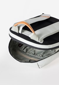 Rucksack mit schwarzem Äußeren und grauen Akzenten, glatter Textur, orangefarbenem Griff und offenem Innenraum mit einer Reißverschlusstasche.