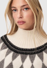 Πουλόβερ από μάλλινο υλικό με ψηλό ραμμένο γιακά, διαθέτει καφέ και κρέμα διαμαντένιο σχέδιο, μαύρη ταινία γύρω από τον λαιμό, απαλός υφής.