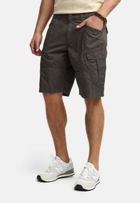 Cargo shorts i mørkegrå stof med flere lommer, afslappet pasform og syninger. Sammen med hvide sportsko.