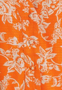 Tissu à motif floral orange avec des fleurs blanches, présentant une surface texturée et un petit bouton de fermeture au centre.
