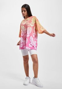 Oversized short-sleeve shirt in gradient pink and orange with white floral patterns, paired with white bike shorts and white sneakers.