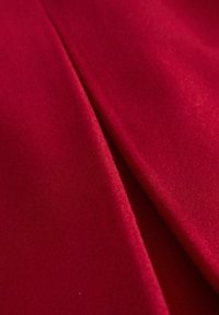Roter Wollstoff mit glatter Textur, der den Fall und den leichten Glanz zeigt, mit einer gefalteten Ecke. Keine sichtbaren Muster oder Beschläge.