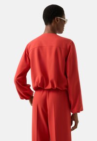 Rød, letvægts langærmet top med rund halsudskæring og elastisk talje, kombineret med matchende højtskårne bukser. Glat tekstur.