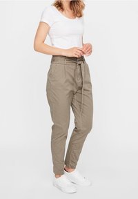 Pantalons en khaki légers à taille haute, avec un nœud de ceinture, des jambes fuselées et des poches latérales, associés à un t-shirt blanc ajusté et des baskets blanches.