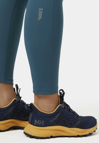 Turquoise legging met reflecterend logo-detail, gecombineerd met marineblauwe en gele schoenen met mesh stof, ingewikkeld patroon en gestructureerde zool.