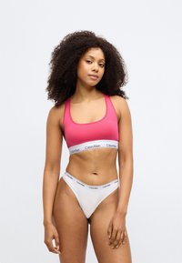 Σπόρ μπρα πουα από τον Calvin Klein σε φωτεινό ροζ με πλατύ μαύρο λογότυπο στη ζώνη; συνδυασμένο με λευκό θρασύσχρονο εσώρουχο που περιλαμβάνει σχέδιο σε αντίθεση στη ζώνη.