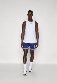 Vitt ärmlöst linne med svart logotyp, blå sportshorts med grå detaljer och Los Angeles-logotyp, vita strumpor och svarta och vita sneakers.