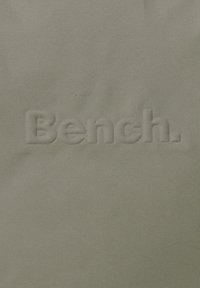 Tissu vert clair avec un logo brodé en relief portant le mot "Bench." avec une texture lisse et mate. Pas d'autres motifs ou accents.