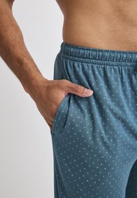 Blaue gemusterte Loungehosen mit einem elastischen Bund und seitlichen Taschen. Der Stoff hat kleine, kontrastierende hellblaue Punkte.