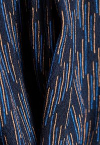 Tessuto navy caratterizzato da linee verticali blu e oro. La texture è liscia con un leggero lucido, che mette in risalto un motivo moderno.