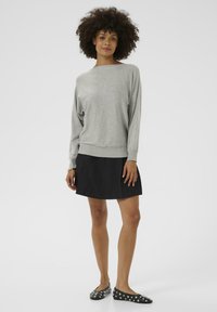 Gray long-sleeve sweater with a wide neckline, paired with a black pleated skirt. Black flats feature silver studs. Smooth texture.