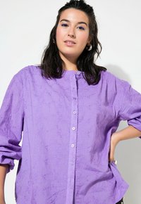Camicia a pulsante viola con un motivo floreale testurizzato e vestibilità rilassata. Presenta maniche lunghe e scollatura rotonda.