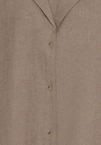 Chemise en lin marron boutonnée avec un col cranté, montrant un gros plan de la texture du tissu et trois boutons beige sur le devant.