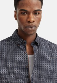 Marineblaues Hemd mit geometrischem Muster in Weiß und Hellblau, im Button-Up-Stil, mit Kragen und abgerundetem Saum. Der Stoff wirkt glatt.