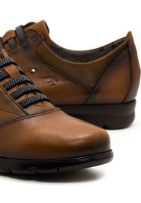 Zapatos de cuero marrón con punta redonda, que presentan cordones gris oscuro y una suela acolchada negra. Textura suave con un ligero brillo.